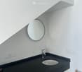 Modern bathroom with a black countertop, white sink, chrome faucet, and round mirror on the wall.