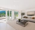 Modern living room with large windows offering a scenic view, a grey sofa with throw pillows, a black coffee table, a floor lamp, and a fireplace.