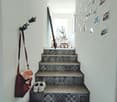 Staircase with patterned tiles, white walls, and a small plant visible at the top. Shoes and a bag are placed on the stairs.