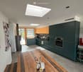Open-plan kitchen and dining area with dark green cabinets, wooden dining table, and modern appliances.