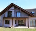 Two-story house with a modern design, featuring a tiled roof, large windows, and a balcony on the upper level.
