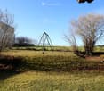 A grassy yard with a swing set, bare trees, and a fence surrounding the area.