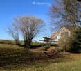 A grassy yard with trees, a swing set, and a house with a red-tiled roof in the background.