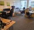 Office space with desks, chairs, computers, a printer, and a small plant on a desk.