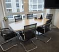 Conference room with a round table, six black chairs, a large flat-screen TV, and a small potted plant near the window.