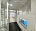 Modern hallway with glass walls, carpeted floor, and recessed lighting. Features a door leading to another room and a visible interior space beyond.