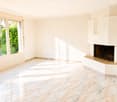 Empty room with white walls, marble tiled floor, large windows with greenery view, and a built-in fireplace.