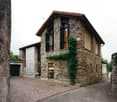 Two-story stone house with a garage, large windows, and ivy climbing on the walls.