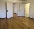 Empty room with wooden flooring and white walls, featuring multiple open doors leading to adjacent spaces.