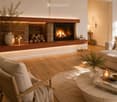 Modern living room with a fireplace, wooden flooring, a sofa, a chair, a coffee table, and decorative items including books and candles.