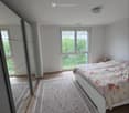 Bright bedroom with wooden flooring, large window, bed with floral bedding, and patterned rug.