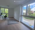 Bright room with wooden flooring, large windows, a chair, a table with a laptop, and a small rug.