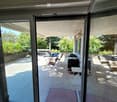 Spacious balcony with tiled floor, glass sliding doors, outdoor furniture including a table, chairs, grill, and small stool.