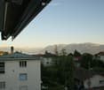 Balcony view overlooking a residential area with houses, trees, and distant mountains under a clear sky.