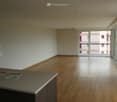 Empty room with wooden flooring, large windows, and a balcony access. No furniture or equipment present.