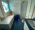Bathroom with white tiled walls, blue tiled floor, sink, toilet, cabinet, and a small plant on the windowsill.