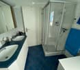 Modern bathroom with two sinks, a large mirror, a glass-enclosed shower stall, and a blue towel hanging on the side.