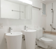 Modern bathroom with white tiles, a large mirror, a sink, a toilet, and a bathtub with a showerhead.