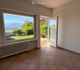 Empty room with white walls, brown tiled floor, large windows, and a white radiator.