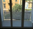 Balcony with large glass doors, white tiled floor, metal railing, and view of surrounding buildings and greenery.