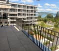 Balcony with modern metal railing, overlooking a multi-story residential building and a scenic lake view.