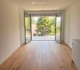Empty room with light wooden flooring, white walls, and large glass sliding doors leading to a balcony with outdoor view.