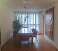 Dining room with wooden parquet flooring, a large wooden dining table surrounded by red chairs, a large painting on the wall, and a potted plant near the window.