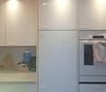 Modern kitchen with white cabinets, a built-in oven, and a refrigerator. The counter has various items including a kettle, bottles, and a bag.