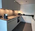 Modern kitchen with white cabinets, dark countertops, and stainless steel appliances including a coffee machine, microwave, and oven.