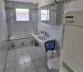 Modern bathroom with a bathtub, double sink, toilet, mirror, and towel rack. Features tiled walls and floor, with a window providing natural light.