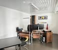 Modern office space with a wooden desk, ergonomic chair, computer setup, floor lamp, and a small meeting table.
