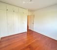 Empty room with light-colored walls, polished wooden flooring, and built-in white closet units. A door leads to another space.