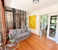 Modern living room with hardwood flooring, grey sofa, glass coffee table, potted plant, and a staircase leading to an upper level.