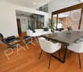 Modern living and dining area with wooden flooring, white sofa, leather chair, and a wooden dining table with four white chairs.