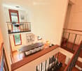 Open-plan interior with a staircase leading to a loft area, featuring a dining table with chairs, a bed in the loft, and a small seating area with stools and a table.