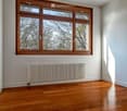 Empty room with wooden flooring, large wooden-framed windows, and a radiator against one wall.
