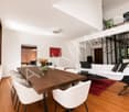Modern living and dining area with white walls, wooden flooring, a white sofa, a coffee table, a wooden dining table with chairs, and a vase with flowers on the table.