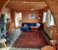 Cozy living room with wooden walls and ceiling, stone floor, fireplace, blue sectional sofa, coffee table, and a colorful rug.