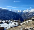 A cluster of houses and buildings in a snowy mountain valley, surrounded by snow-covered peaks and trees.
