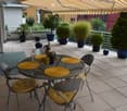 Balcony with a round metal table, four chairs, wine bottle, wine glasses, plates, and potted plants.