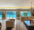 Elegant living room with large windows offering a scenic lake view, featuring a beige sectional sofa, coffee table, chandelier, side tables, and mirrors.