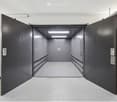 Corridor / Hallway. A modern, clean hallway with a large, open garage door leading to a spacious, well-lit garage area. The hallway features a smooth, light-colored floor and white walls, with a sleek, contemporary design.