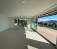 Empty room with large glass sliding doors leading to a balcony, offering a scenic view of the landscape and city.
