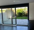 Empty room with dark tiled flooring, large sliding glass doors leading to a garden, and a small black table with a remote control on it.