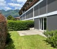 Well-maintained garden with a trimmed hedge, neatly mowed lawn, and a modern house with large windows and a view of mountains in the background.