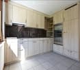 Modern kitchen with light wood cabinets, stainless steel oven, and tiled floor.