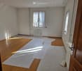 Empty room with wooden flooring, white walls, and large windows with curtains. No furniture or equipment present.