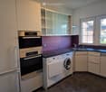 Modern kitchen with white cabinets, stainless steel appliances, and a dark countertop. Features include a refrigerator, oven, dishwasher, washing machine, and a sink with a faucet.