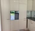 Modern kitchen with white cabinets, a dark countertop, and a built-in oven with a glass door. The floor is made of light wood.