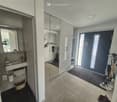 Modern hallway with tiled flooring, large mirror, and adjacent bathroom area visible. Features a sink, mirror, and cleaning supplies in the background.